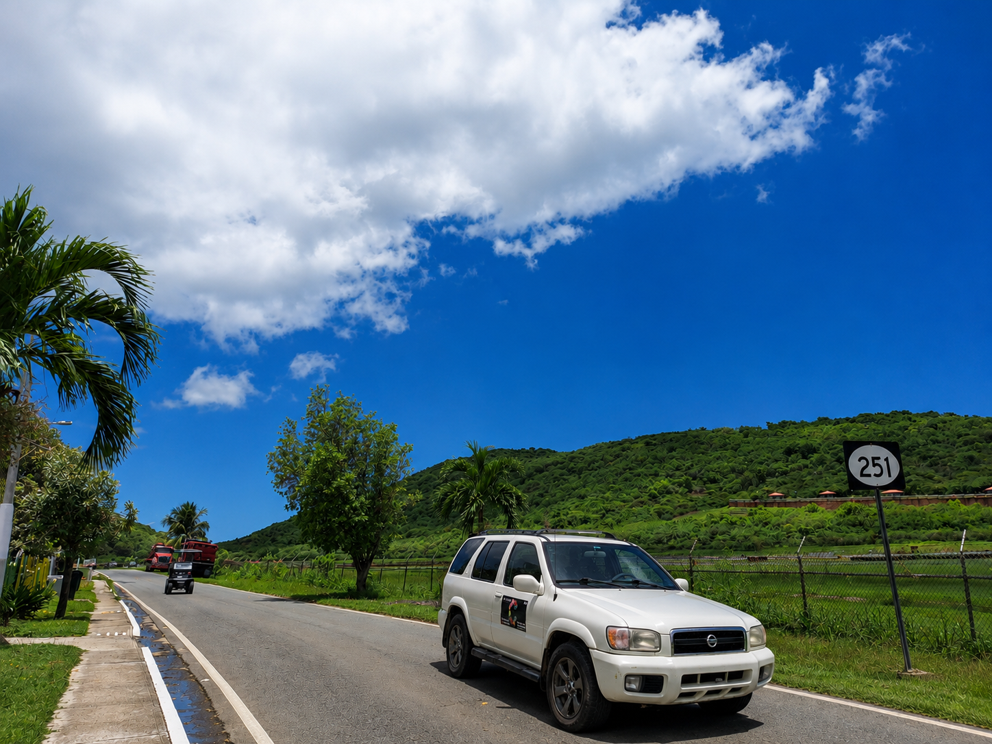 White 2004 Nissan Pathfinder with the Casa Carmen logo on a sunny Culebra road beside green hills