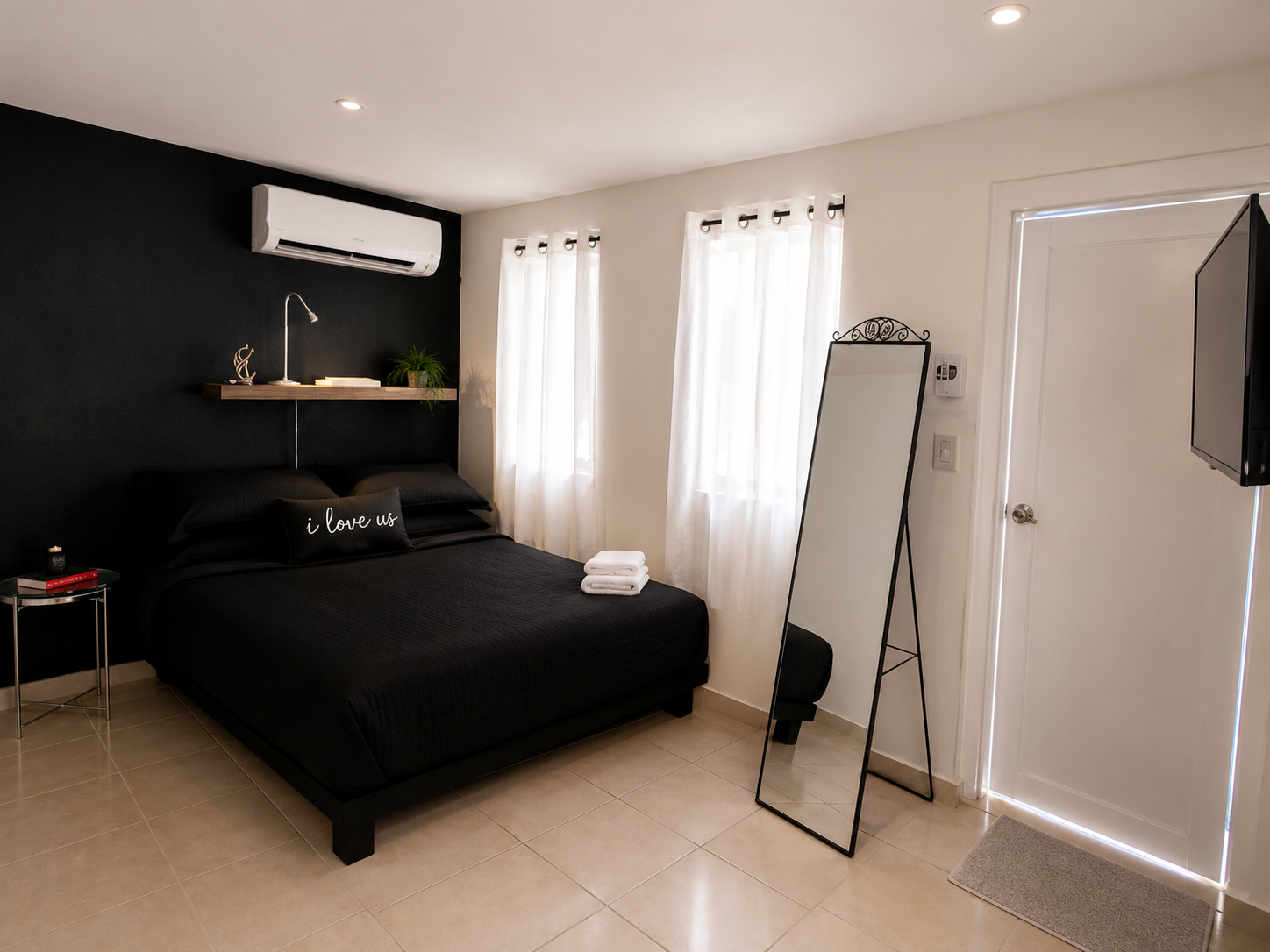 Bedroom with a queen bed against a black accent wall, air conditioning, mirror and bright curtained windows