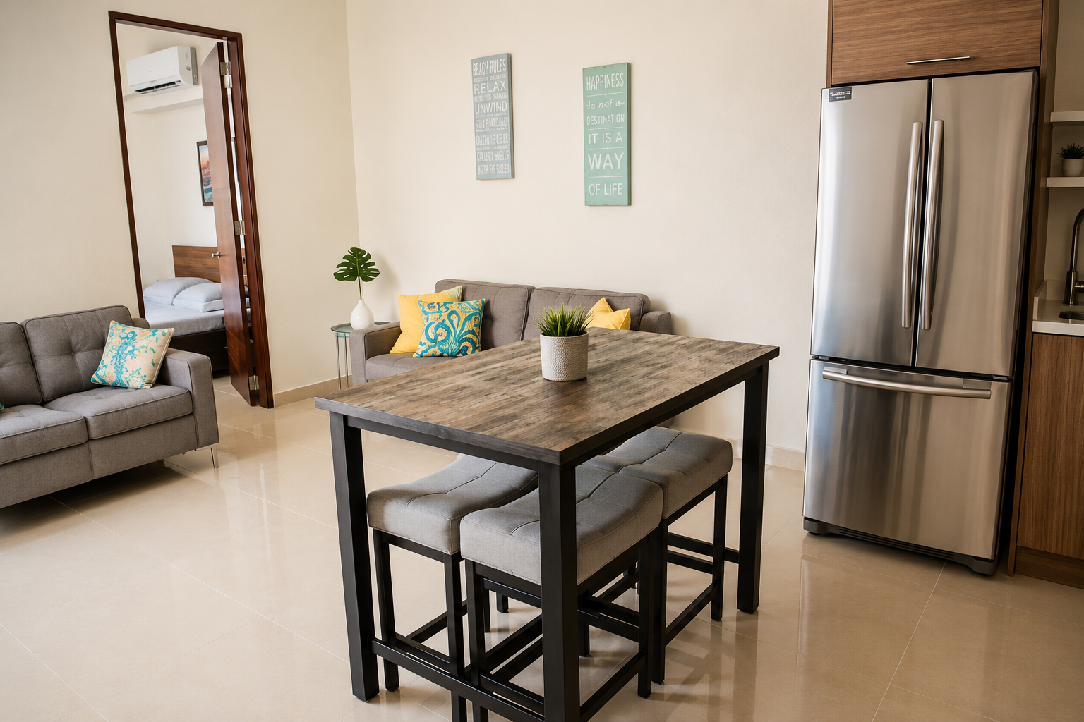 Dining area with high-top wooden table and stools beside a living room with grey sofas
