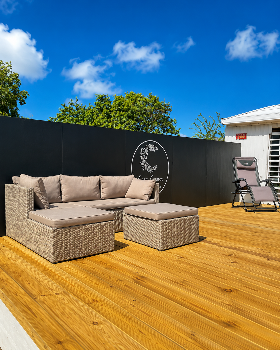 Private outdoor wooden deck with wicker sectional seating and a lounge chair under a blue sky