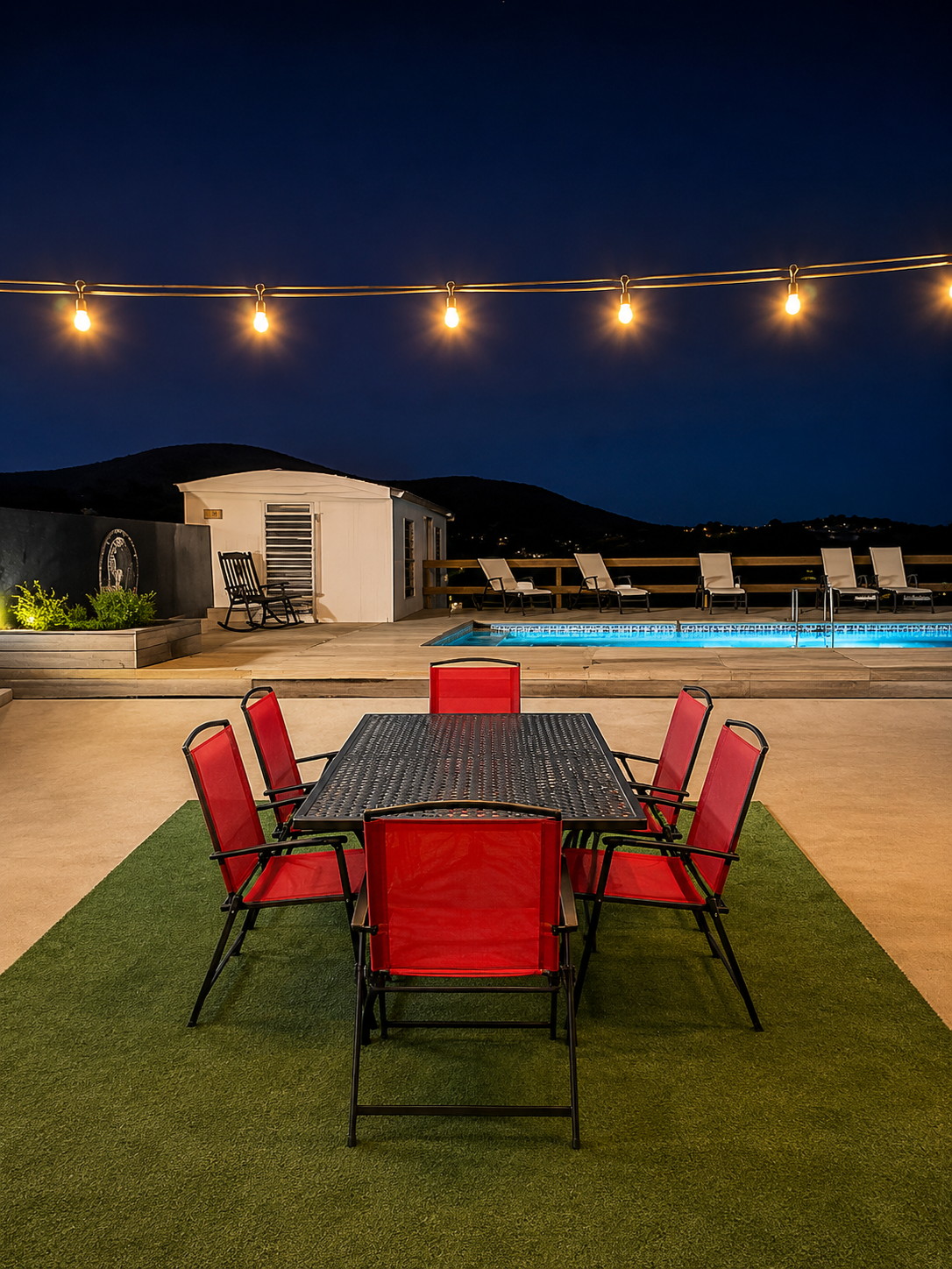 Backyard pool area at night with string lights, outdoor dining table and loungers