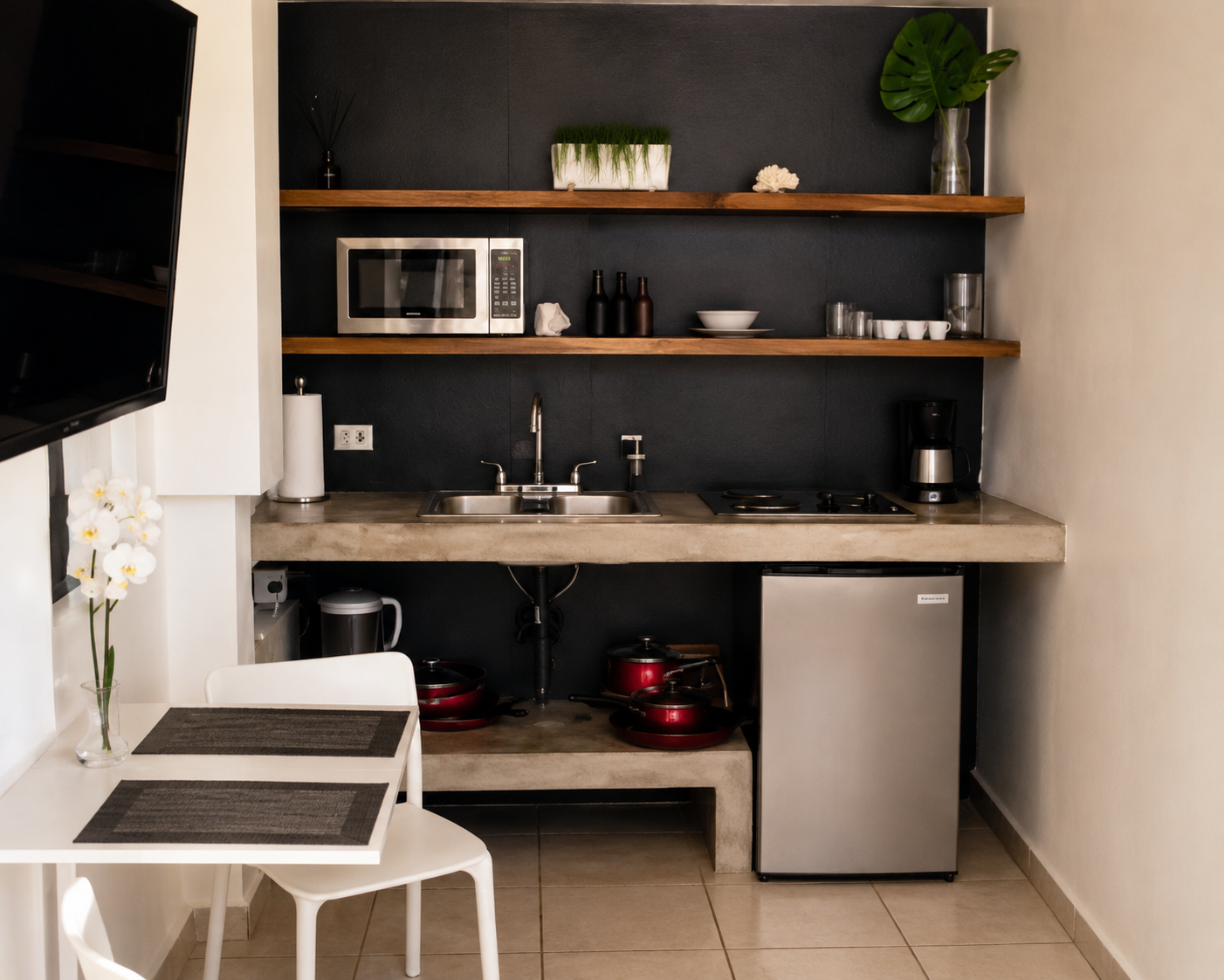 Kitchenette with concrete counter, sink, cooktop, microwave and a white dining table for two